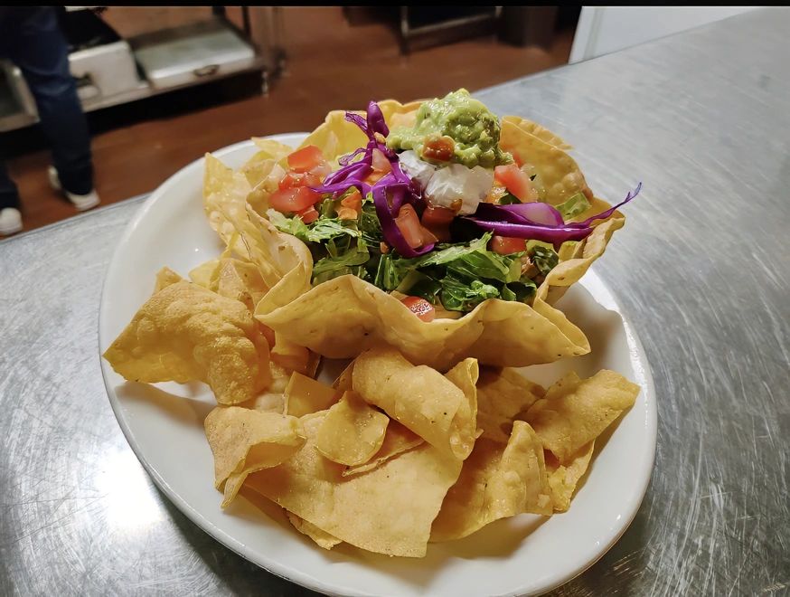 Taco Salad A delicious flour tortilla bowl fried crisp and served with refried beans, lettuce, tomato, cabbage, carrots, cheddar and Monterey jack cheese, black olives, sour cream, and guacamole. Smothered in chile verde or enchildada sauce.